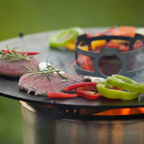 Round solid steel cooking plate featuring sizzling bell peppers, mushrooms, and seasoned meat over an open flame, perfect for camping and farm, garden & tool activities.