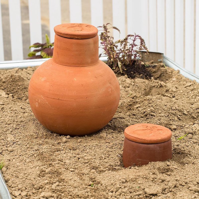 Unglazed terra cotta irrigation pots buried in soil for slow water release, handcrafted and ideal for conserving water in small garden beds and containers, featured in Farm, Garden & Tool and Garden Accessories collections.