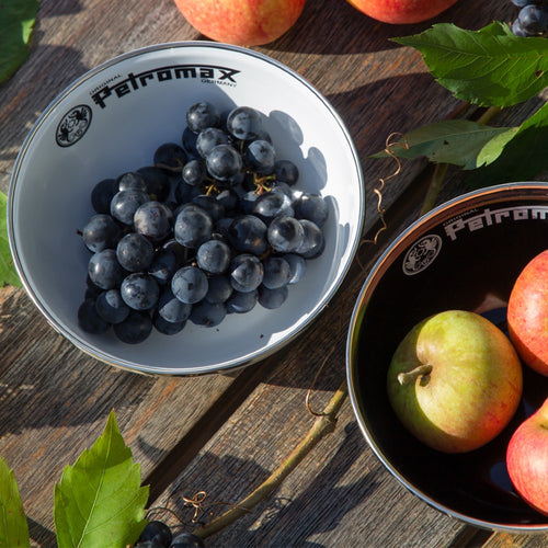 White enamel Petromax bowl filled with dark grapes alongside black enamel Petromax bowl holding apples, displayed outdoors on a wooden surface with leaves, ideal for Farm, Garden & Tool, Kitchen & Food, Camping, Dinnerware, Best Sellers, and Promo Eligible collections.