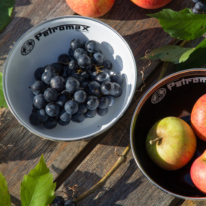 White enamel Petromax bowl filled with dark grapes alongside black enamel Petromax bowl holding apples, displayed outdoors on a wooden surface with leaves, ideal for Farm, Garden & Tool, Kitchen & Food, Camping, Dinnerware, Best Sellers, and Promo Eligible collections.