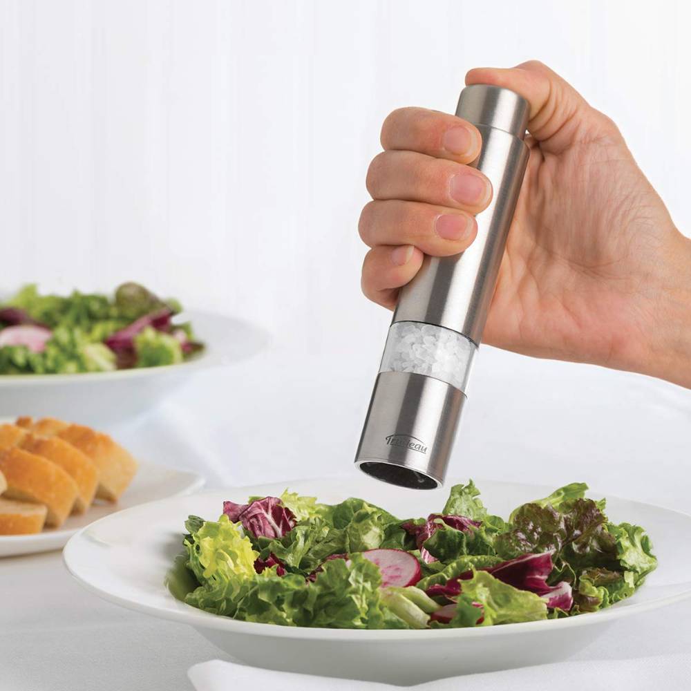 Hand holding a stainless steel one-hand salt mill grinding coarse salt onto a fresh green salad, suitable for Kitchen & Food, Pantry, and Kitchen Gadgets collections.