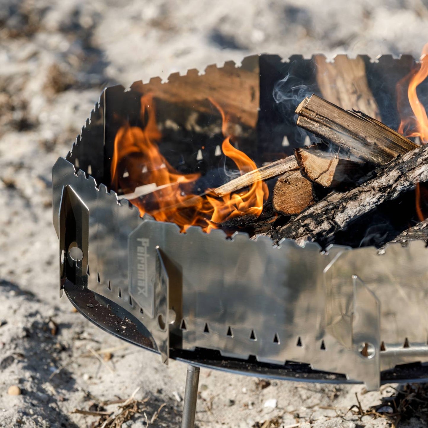 Metal wind shield surrounding burning firewood, designed to protect outdoor cooking setups like fire bowls and Dutch ovens, ideal for Farm, Garden & Tool, Camping, Best Sellers, and Promo Eligible collections.