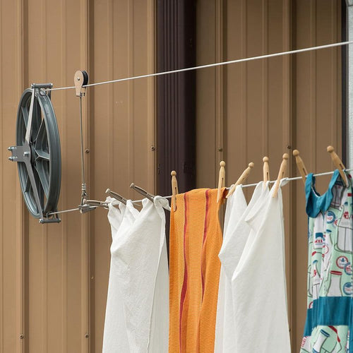 Amish made durable aluminum pulley clothesline system with ball bearing hubs, supporting a 150 ft span, hanging towels and clothes with wooden clothespins in an outdoor laundry setting.