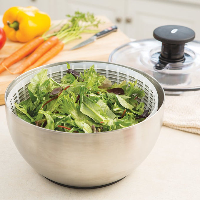 Brushed stainless steel salad spinner bowl filled with fresh mixed greens, featuring a clear locking lid with black push-button handle nearby on kitchen counter, ideal for Kitchen & Food, Kitchen Gadgets, Cooking and Baking Helpers, Best Sellers, and Promo Eligible collections.