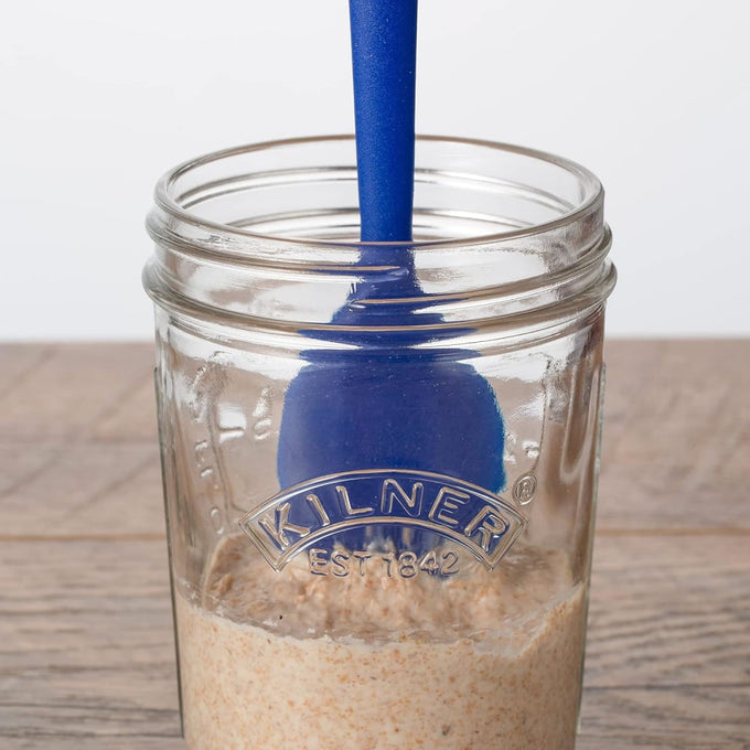 Clear glass jar branded Kilner with sourdough starter and blue silicone spatula on rustic wood surface, showcasing handcrafted kitchen tools in Baking Supplies and Cookware collections.