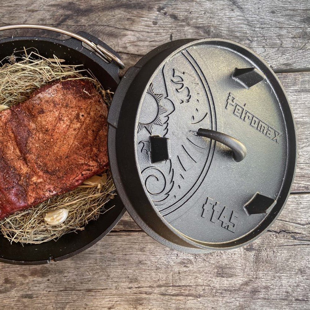 Handcrafted cast iron Dutch oven with flat base, lid featuring sun and swirl embossing, containing seasoned meat and garlic on hay, Kitchen & Food, Cookware, Cast Iron, Best Sellers, Promo Eligible collections.