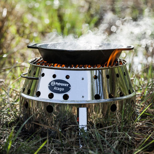 Cast iron Petromax fire skillet with two side handles steaming on a compact outdoor stove, ideal for camping, farm, garden, kitchen, cookware, and cast iron collections.