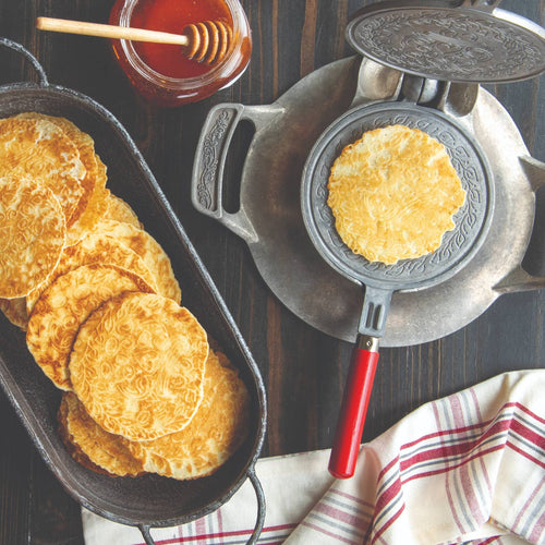 Handcrafted stovetop krumkake iron with aluminum base and red wooden handle, making patterned crisp cookies, featured in Kitchen & Food, Cookware, Baking Supplies, and USA Made collections.