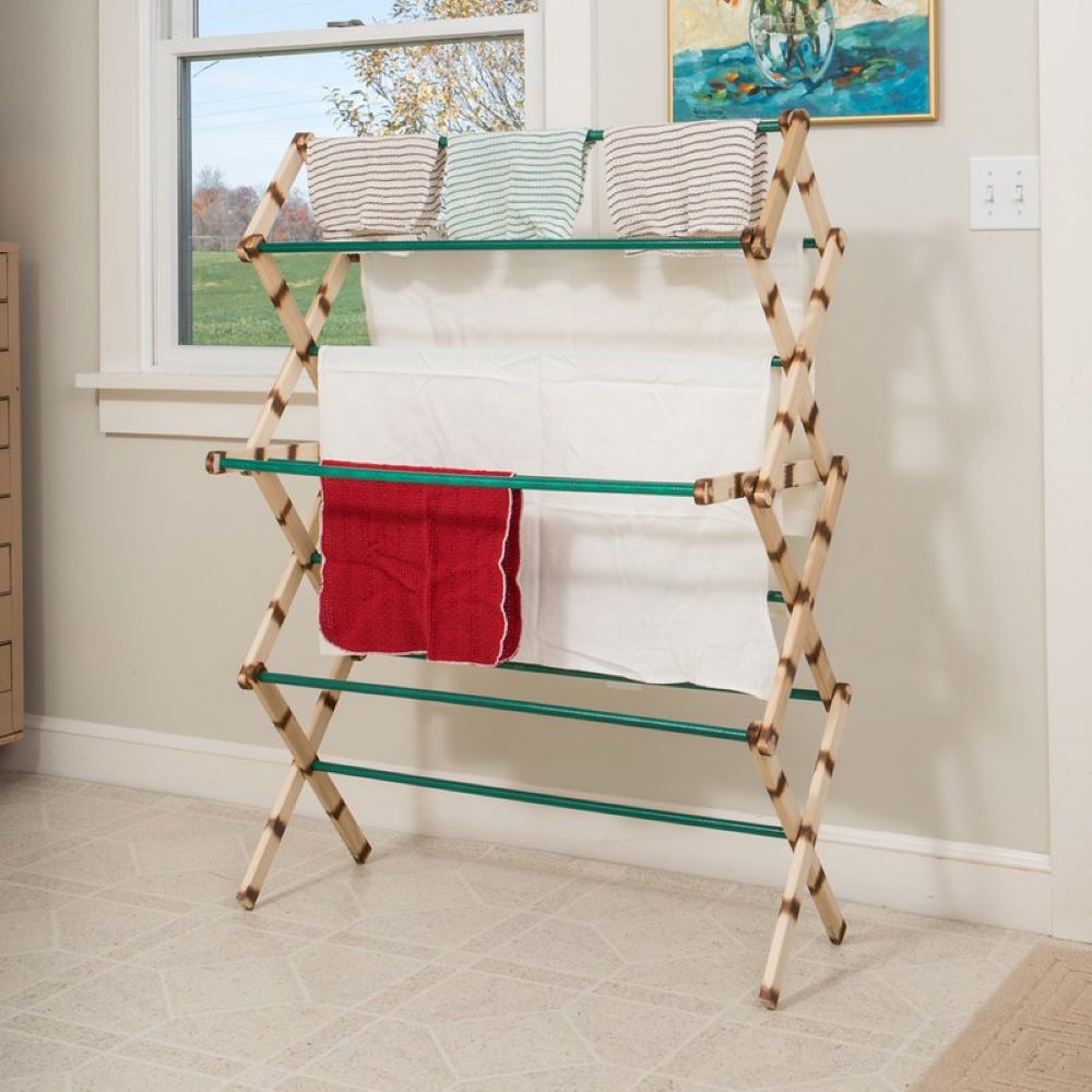 Wooden 11-rung freestanding clothes dryer with green metal rods, holding folded and hanging towels in a bright indoor laundry space, made in USA, ideal for small homes and porches.