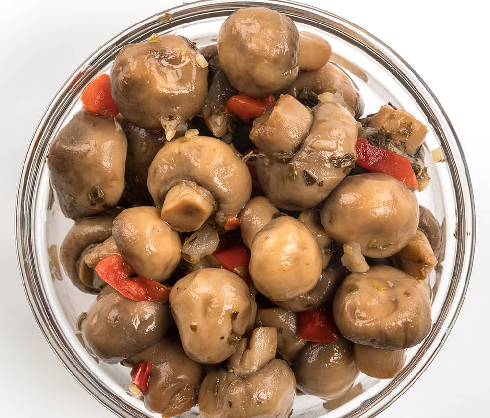 Clear glass bowl filled with marinated whole mushrooms mixed with pieces of red pepper and onions, hand-prepared with natural ingredients, featured in Kitchen & Food and Pantry collections.