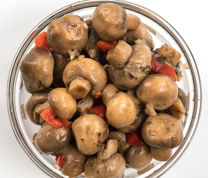 Clear glass bowl filled with marinated whole mushrooms mixed with pieces of red pepper and onions, hand-prepared with natural ingredients, featured in Kitchen & Food and Pantry collections.