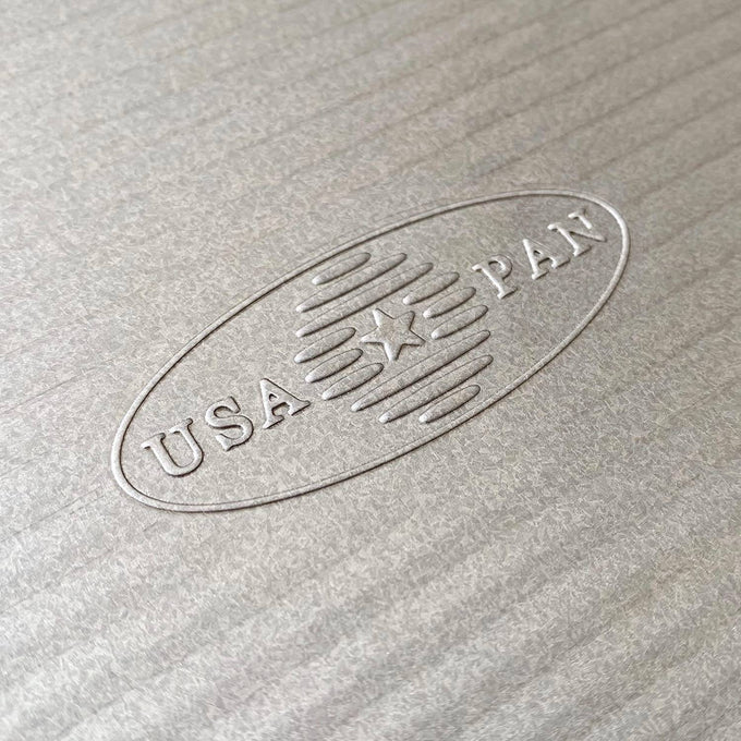 Close-up of an embossed USA Pan logo on a non-stick aluminized steel surface, highlighting its durable construction and American craftsmanship for baking supplies and cookware collections.