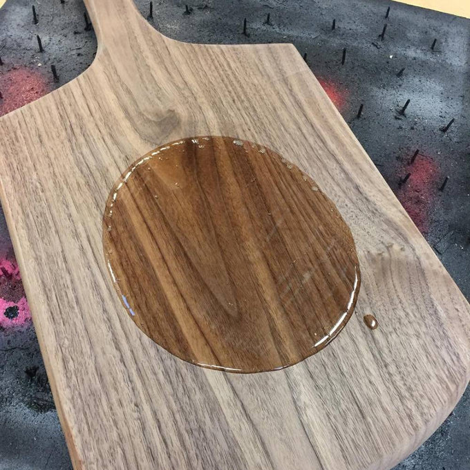 Handmade wooden cutting board with a drop of clear mineral oil soaking into the wood grain, highlighting deep natural tones, ideal for Kitchen & Food and USA Made collections.