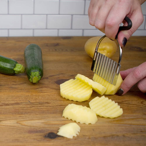 Vintage-style crinkle cutter slicing a peeled potato into decorative waffle fries on a wooden cutting board, featuring an 18/10 stainless steel blade and silicone grip, ideal for Kitchen & Food, Food Prep, Choppers and Cutters, and Kitchen Gadgets collections.