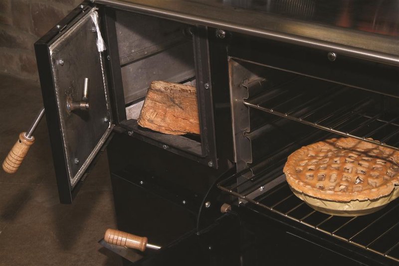 Close-up of the cast iron firebox door open with firewood inside and a baked pie on the oven rack of the Pioneer Princess Wood Cookstove, handcrafted and featured in Stoves, Cookstoves, Best Sellers, and All Stoves & Appliances collections.