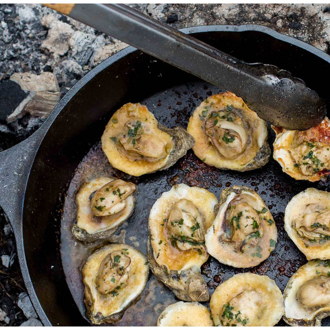 Handcrafted pre-seasoned cast iron skillet cooking oysters with herbs over an open flame, showcasing superior heat retention and durability for Kitchen & Food, Cookware, Cast Iron, Best Sellers, Promo Eligible collections.