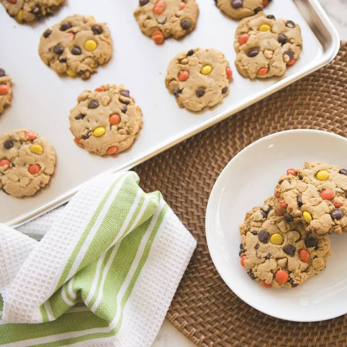 Aluminum half sheet baking pan with lid featuring freshly baked peanut butter cookies with colorful candy pieces, paired with a green-striped kitchen towel and white plate, ideal for Kitchen & Food, Cookware, and Baking Supplies collections.