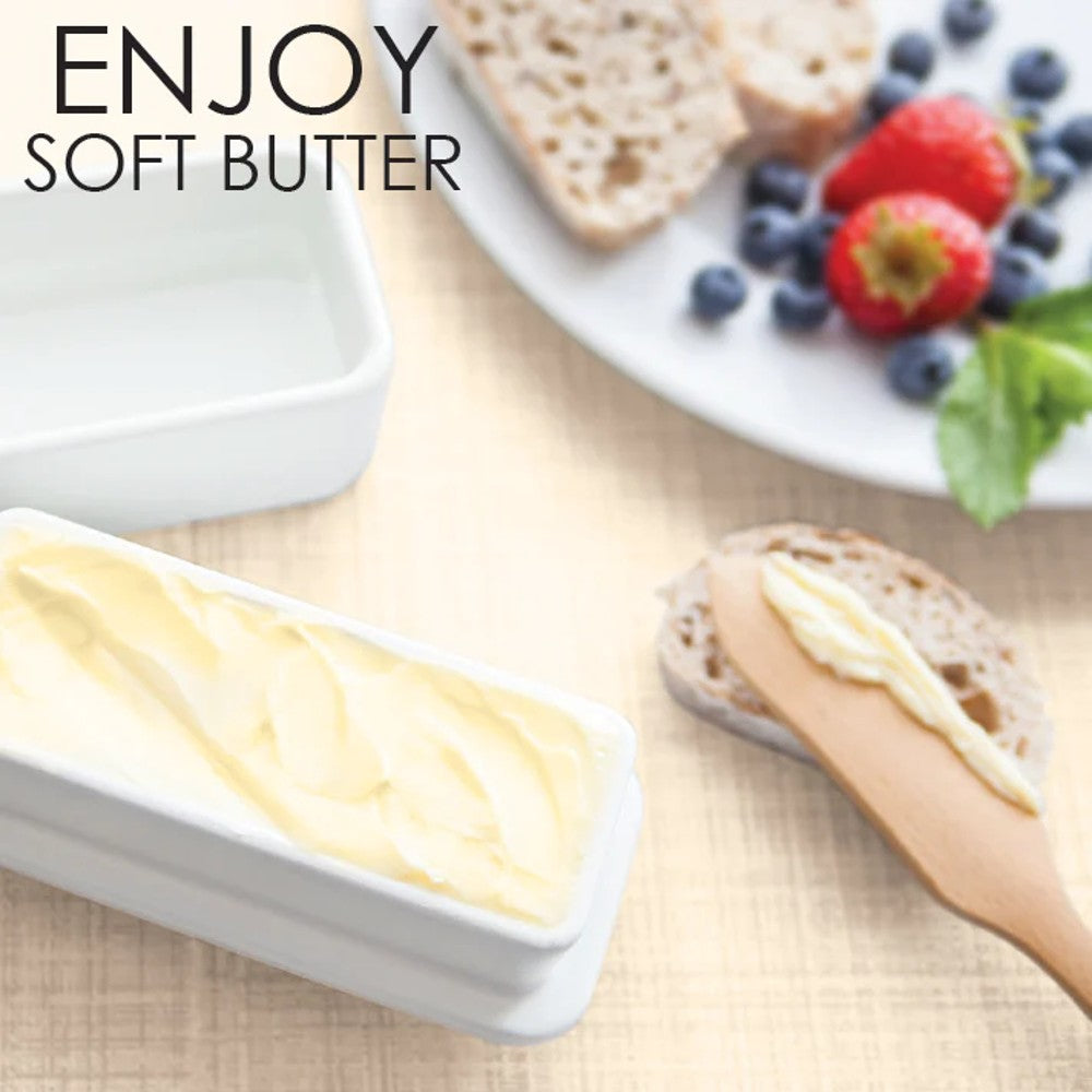 Rectangular white ceramic butter keeper filled with soft spreadable butter, placed near a wooden butter knife and a plate of fresh berries and bread, part of Kitchen & Food and Specialty Equipment collections.