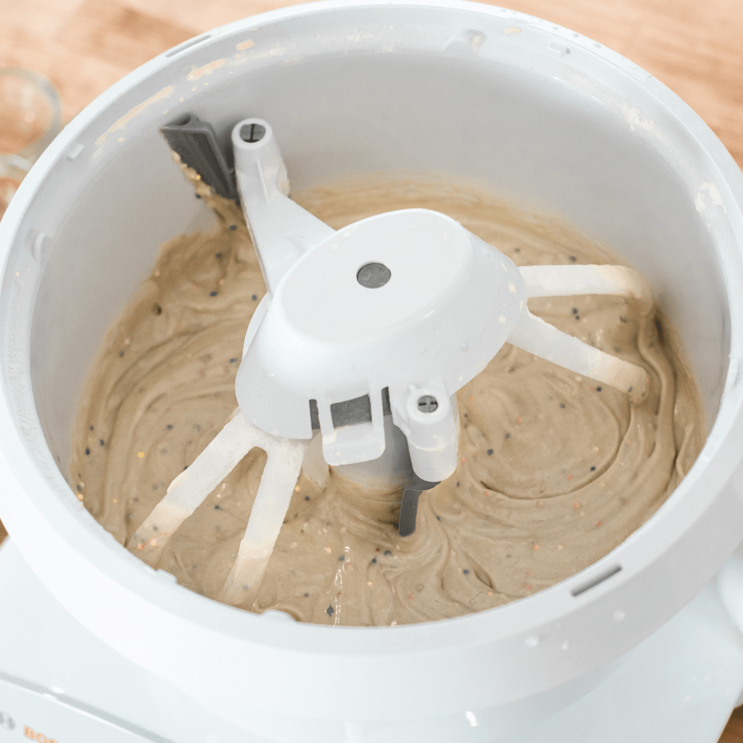 White bowl scraper attachment gently scraping thick batter from the sides and inner post of a mixer bowl, a handcrafted USA made kitchen gadget for baking and cooking helpers collections