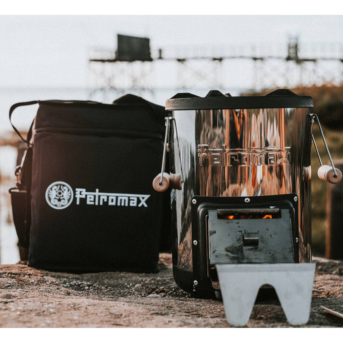 Black ripstop transport bag with reinforced construction and adjustable shoulder strap next to a compact metal outdoor stove, suitable for camping, farm, and garden use.