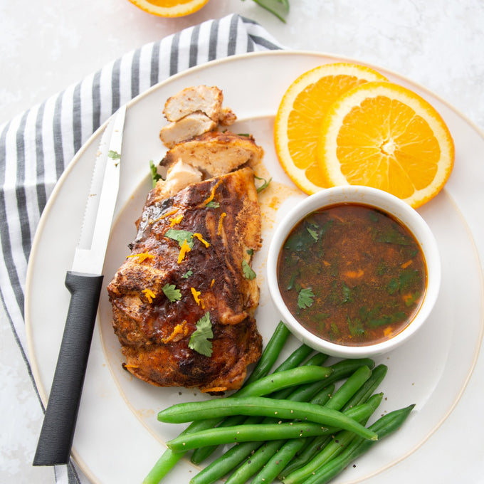 Handcrafted serrated knife with high carbon surgical stainless steel blade and solid black handle alongside sliced seasoned chicken, green beans, orange slices, and dipping sauce, ideal for Kitchen & Food and USA Made collections.