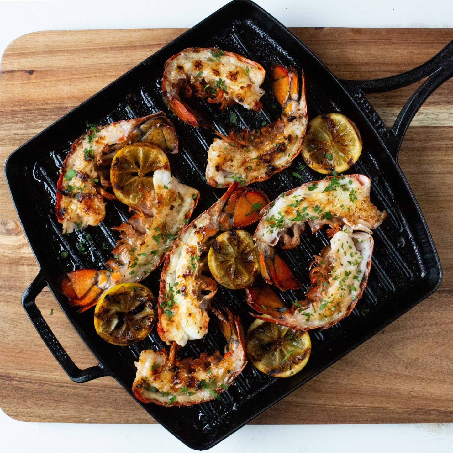 Square cast iron grill pan with grilled shrimp and charred lemon slices, featuring a triple-seasoned, lightweight surface ideal for kitchen and cookware collections made in USA.