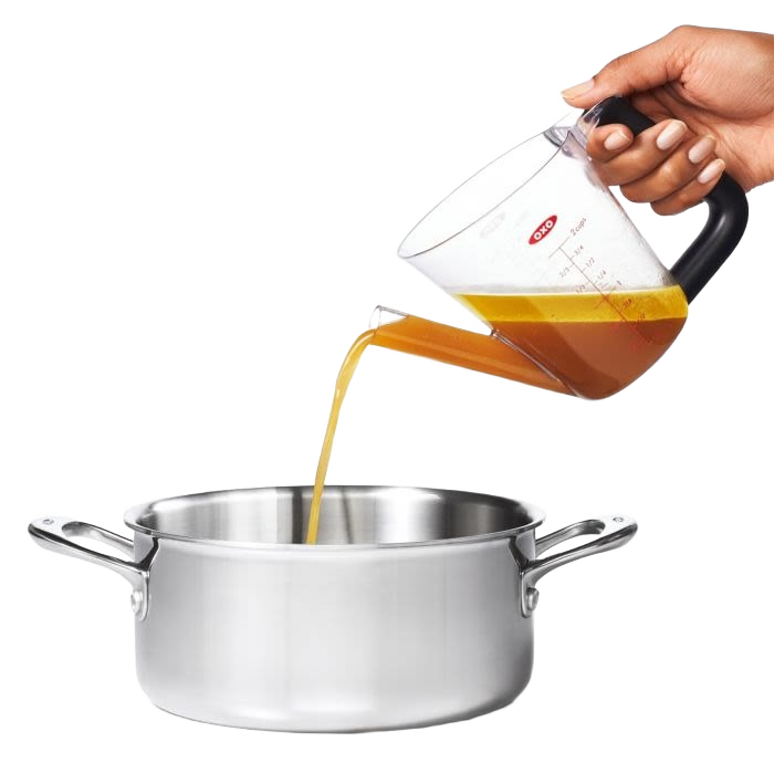 Clear plastic fat separator with a black cushioned grip handle and red stopper, pouring liquid from the spout into a stainless steel pot, ideal for Kitchen & Food and Cooking Helpers collections.
