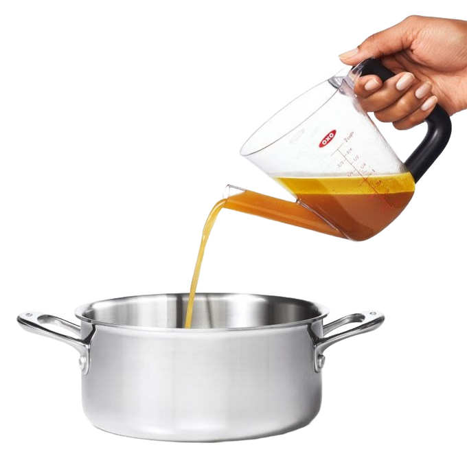 Clear plastic fat separator with a black cushioned grip handle and red stopper, pouring liquid from the spout into a stainless steel pot, ideal for Kitchen & Food and Cooking Helpers collections.