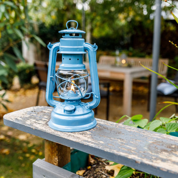 Handcrafted light blue galvanized oil lantern with thermal heat-resistant SUPRAX globe burning softly on a weathered wooden bench, ideal for Lamps & Lighting, Camping, and Emergency Supplies collections.