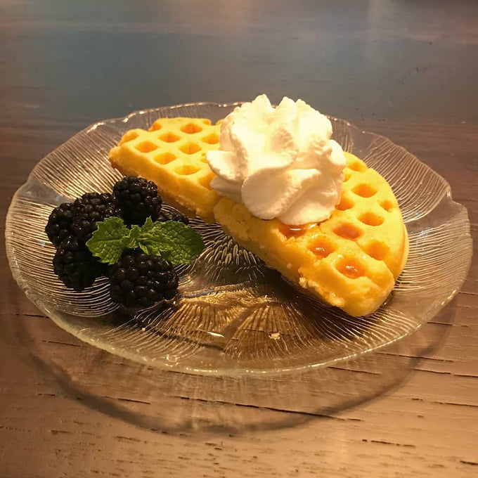 Slice of golden waffle with a crispy edge topped with whipped cream, served on a glass plate alongside fresh blackberries and a sprig of mint, suitable for Farm, Garden & Tool and Kitchen & Food collections.