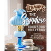 Blue vintage-style oil lamp with a ruffled glass shade placed beside stacks of bowls on a glass table, evoking a nostalgic, handcrafted USA-made lifestyle theme.