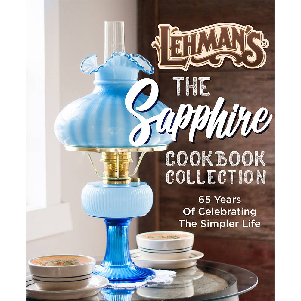 Blue vintage-style oil lamp with a ruffled glass shade placed beside stacks of bowls on a glass table, evoking a nostalgic, handcrafted USA-made lifestyle theme.