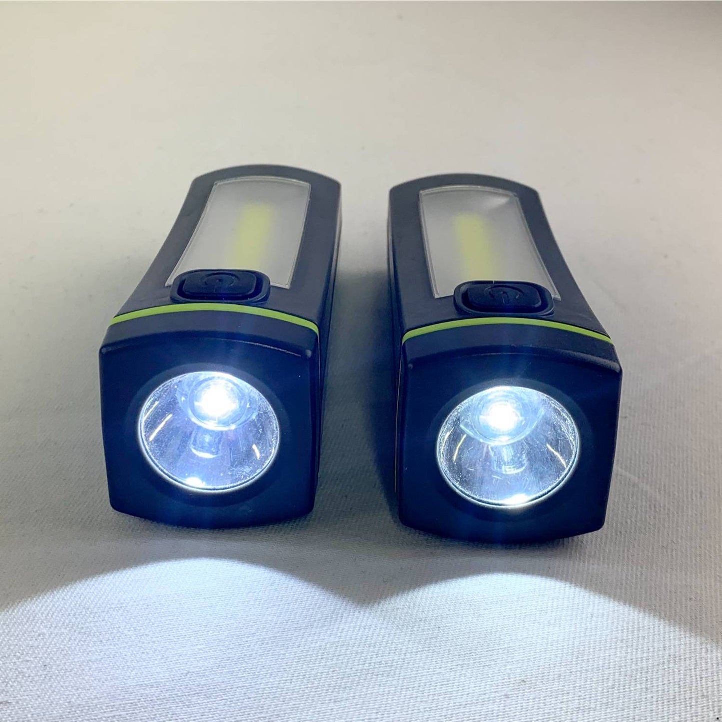 Pair of compact black and green LED flashlights emitting bright white light, designed for use in camping, emergency supplies, and versatile outdoor lighting collections.