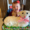 Child enjoying a festive lamb-shaped cake decorated with white frosting, coconut flakes, and a pink ribbon, showcasing a fun Easter baking tradition in Kitchen & Food and Baking Supplies collections.