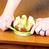 Hands holding a green wedge and pop cutter slicing a red and yellow apple into eight segments on a wooden surface, ideal for food prep in farm, garden, and kitchen collections.