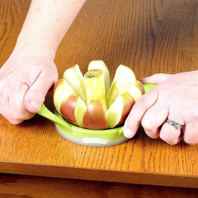 Hands holding a green wedge and pop cutter slicing a red and yellow apple into eight segments on a wooden surface, ideal for food prep in farm, garden, and kitchen collections.