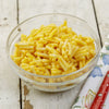 Clear glass bowl filled with creamy prepared macaroni and cheese on a rustic wooden surface next to a floral napkin and red-handled utensil, perfect for pantry and Kitchen & Food collections.