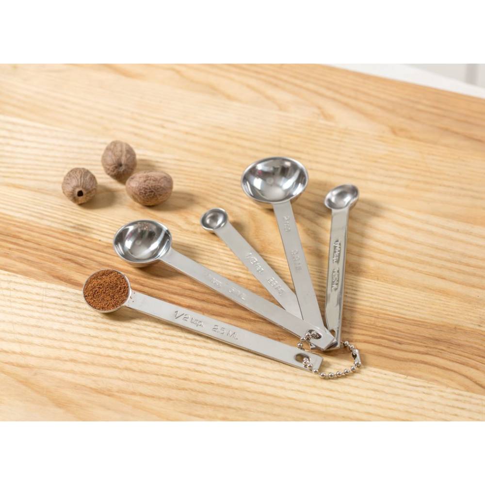 Set of five linked stainless steel measuring spoons with engraved measurements, containing ground spice in one spoon, displayed on a wooden surface with whole nutmegs; featured in Kitchen & Food, Food Prep, Measuring, Best Sellers, and Promo Eligible collections.