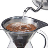 Close-up of water being poured from a stainless steel kettle into a stainless steel micro-filter brewing coffee in a clear glass carafe, ideal for brewing coffee and tea collections.
