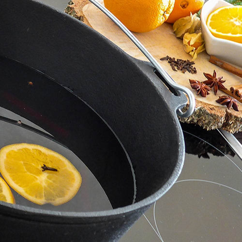 Black cast iron Dutch oven with flat base and bail handle, shown with spiced citrus slices inside, set on stove next to a wooden board with oranges and spices, featured in Kitchen & Food, Cookware, Cast Iron, Best Sellers, and Promo Eligible collections.