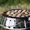 Cast iron pan with 30 mini Dutch pancakes cooking over an open fire on a stainless steel camp stove, designed for outdoor use in camping, kitchen, and cookware collections.