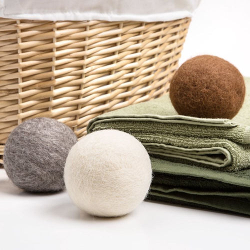Set of three all-natural wool dryer balls in brown, gray, and off-white colors arranged near folded green towels and woven laundry basket, crafted for Laundry Supplies and Home & Decor collections.