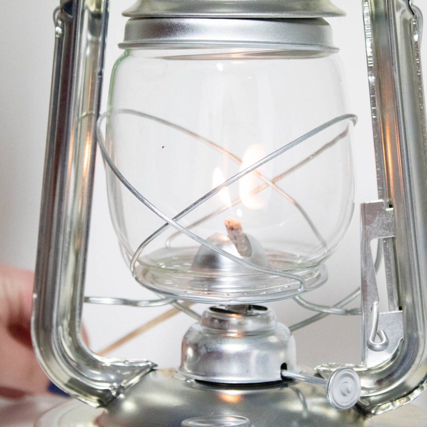 Close-up of a handcrafted Rayo Redi-Lite Lantern burning with a bright flame inside a clear glass globe, featuring durable weather-resistant silver metal frame, ideal for camping and emergency use.