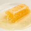Handcrafted pure honeycomb dripping natural raw honey onto a white plate, rich in enzymes and pollen, ideal for Kitchen & Food, Pantry, USA Made, and Best Sellers collections.