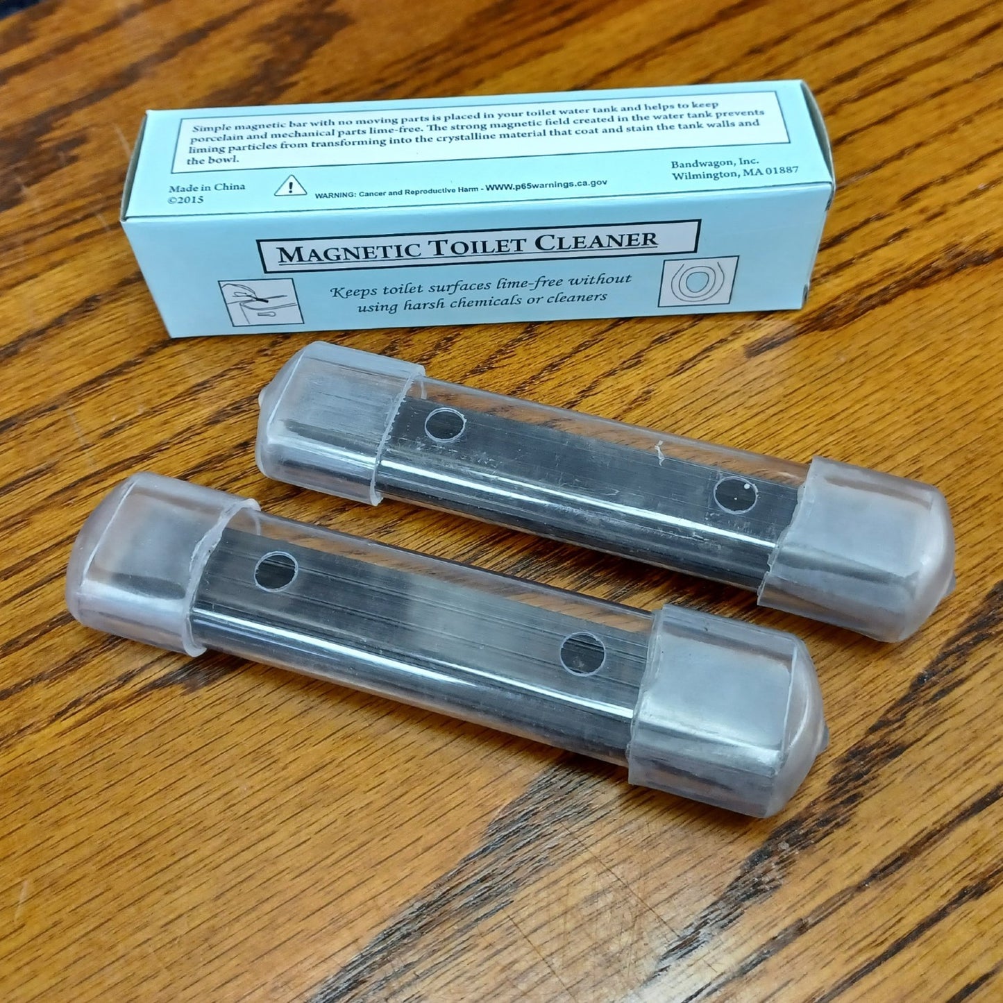 Two clear plastic housings each containing long-lasting magnets designed to prevent mineral buildup and stains in toilet tanks, placed on a wood surface, featured in Home & Decor and Household Cleaning collections.