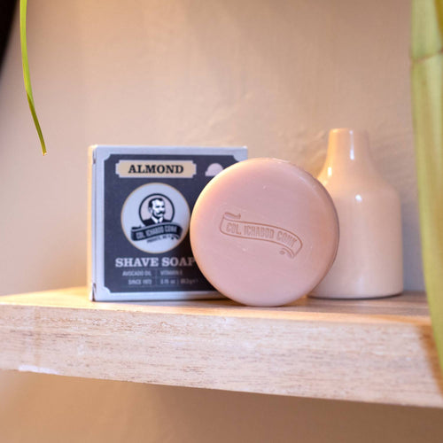 Handcrafted almond-scented shaving soap bar embossed with logo, resting beside its matching box on a wooden shelf, featuring nourishing ingredients, made in USA, part of Health & Wellness, Grooming and Personal Hygiene, Soaps and Soapmaking, USA Made, Best Sellers, and Promo Eligible collections.