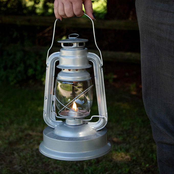 Handcrafted metal lantern with glass globe and protective wire frame, held outdoors, providing steady bright light for farm, garden, camping, and emergency use.