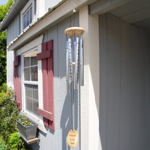 Handcrafted 40-inch silver metal wind chime with wooden top and engraved windcatcher, hanging outdoors on gray siding near window with red shutters, ideal for Farm, Garden & Tool, Garden Accessories, Best Sellers, and Promo Eligible collections.