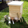 Natural wood 10-frame beekeeping hive with handcrafted essential tools including smoker, hive tool, bee brush, and feeder, displayed outdoors on grass for farm and garden supplies.