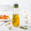 Clear glass oil spray bottle with green-accented top, filled with golden oil and herbs, ideal for precise low-fat cooking and grilling in Kitchen & Food, Cookware, and Baking Supplies collections.